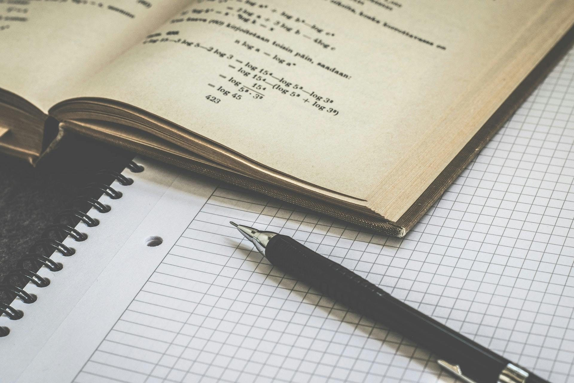 A mathematics textbook next to a pen and notepad.